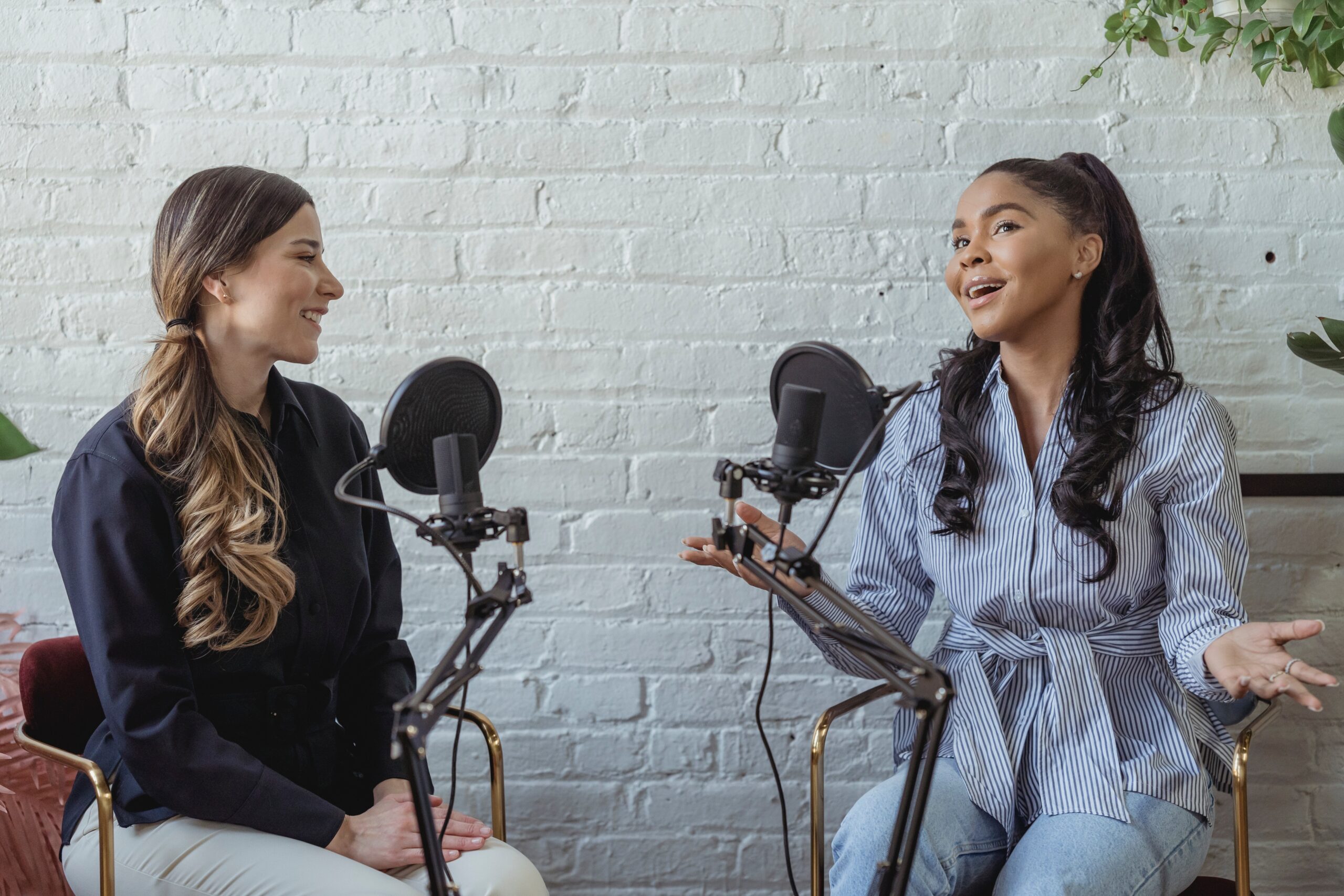 Image of two women speaking and smiling into microphones on a podcast 
