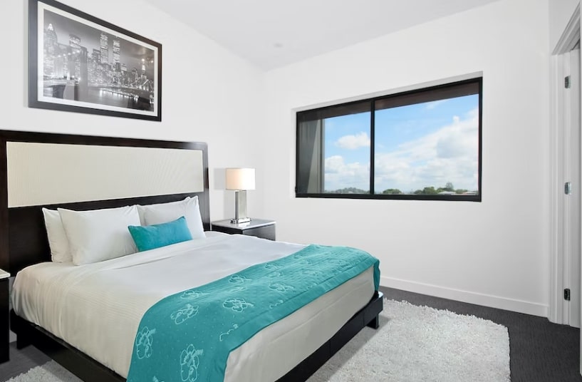 A bed in a modern furnished bedroom with a picture above and view of blue sky from the window 