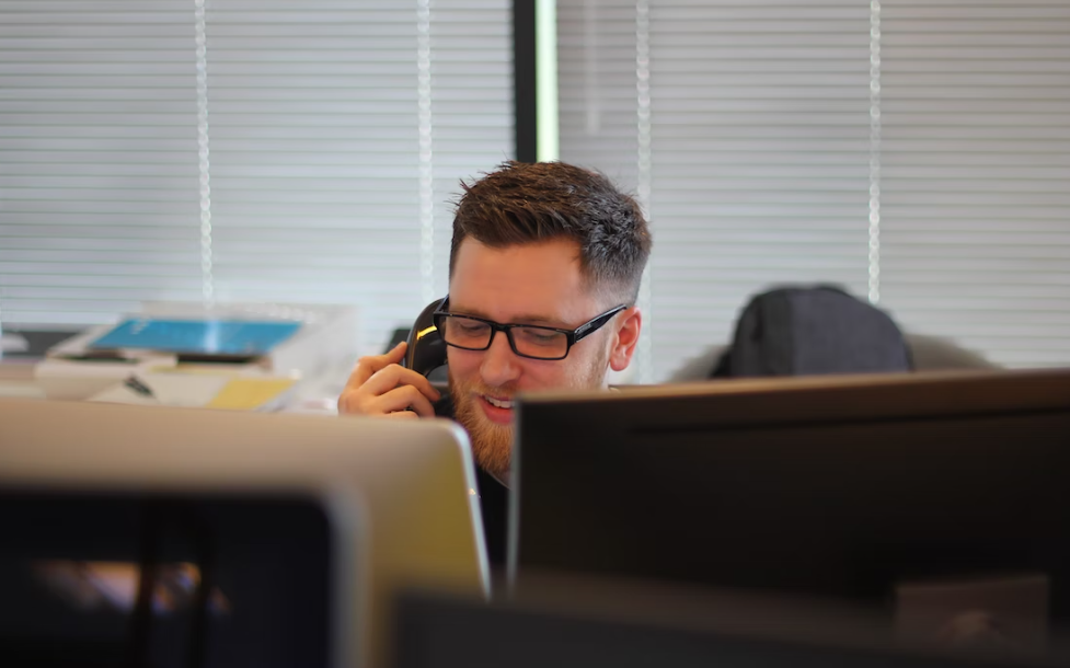 A cusotmer service agent answering a phone call with two computer screens in front of him