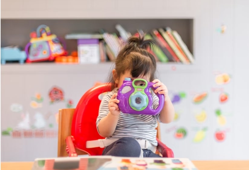 A small girl sitting in a high chair and playing with a toy 