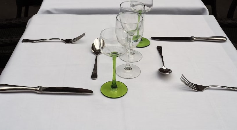A table with cutlery and wine glasses laid on a white tablecloth 