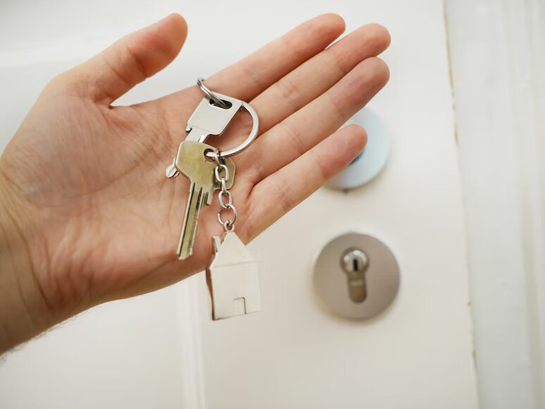 A hand holding the keys with a door and keyhole in the background 